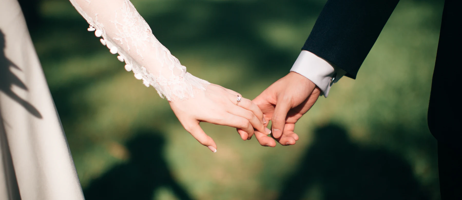 Two people holding hands, one in a lace sleeve and one in a dark suit