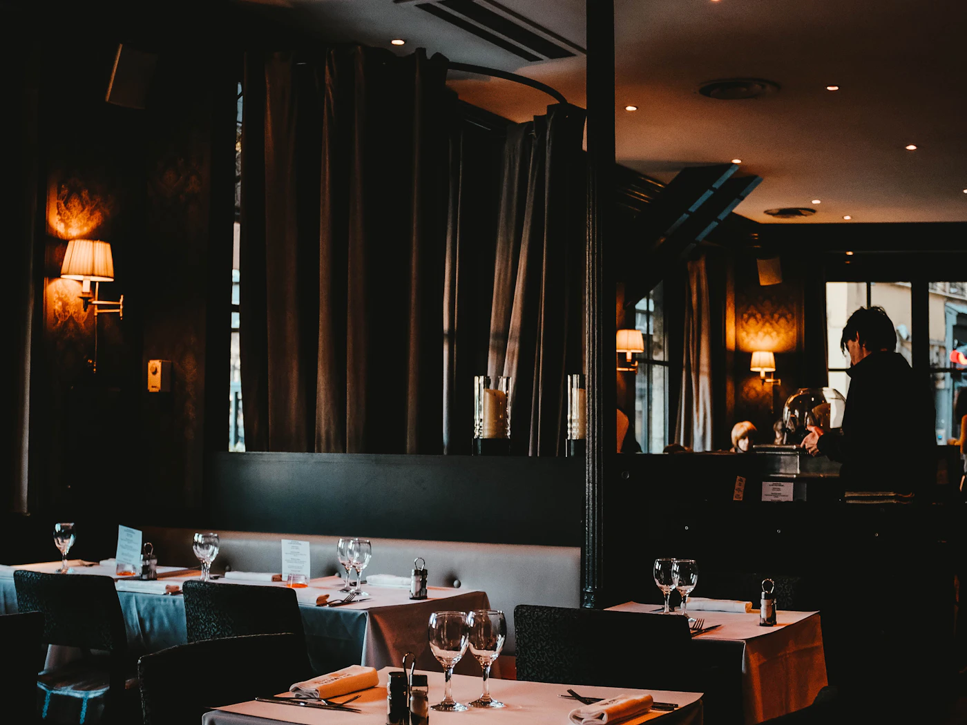 A dim private dining room with laid tables and warm wall lights