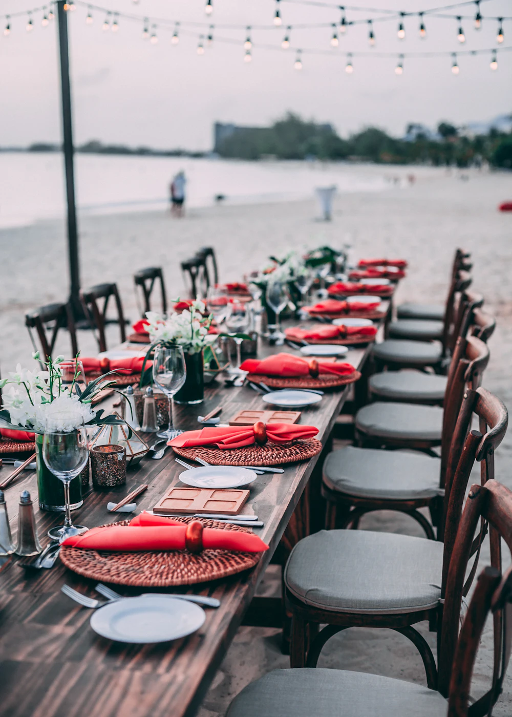 A long outdoor table dressed with red napkins, flowers and string lights