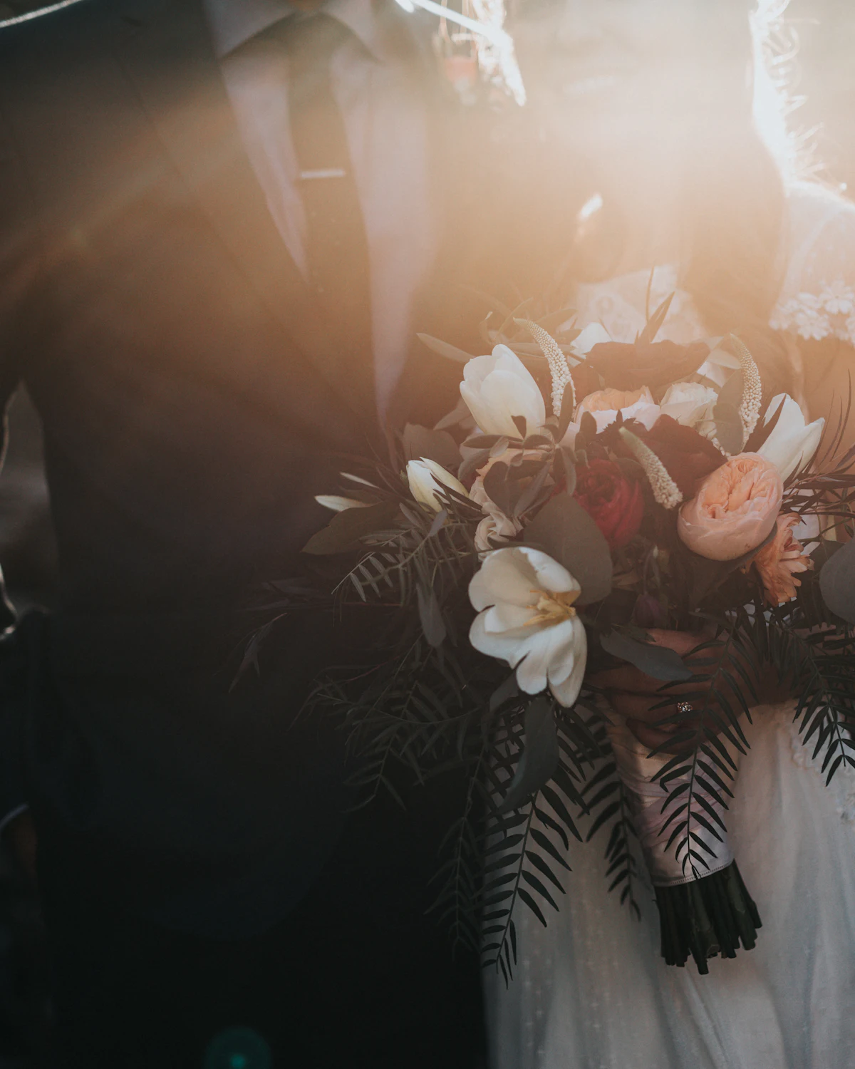 A floral bouquet held between two people in formal dress, lit by low sun