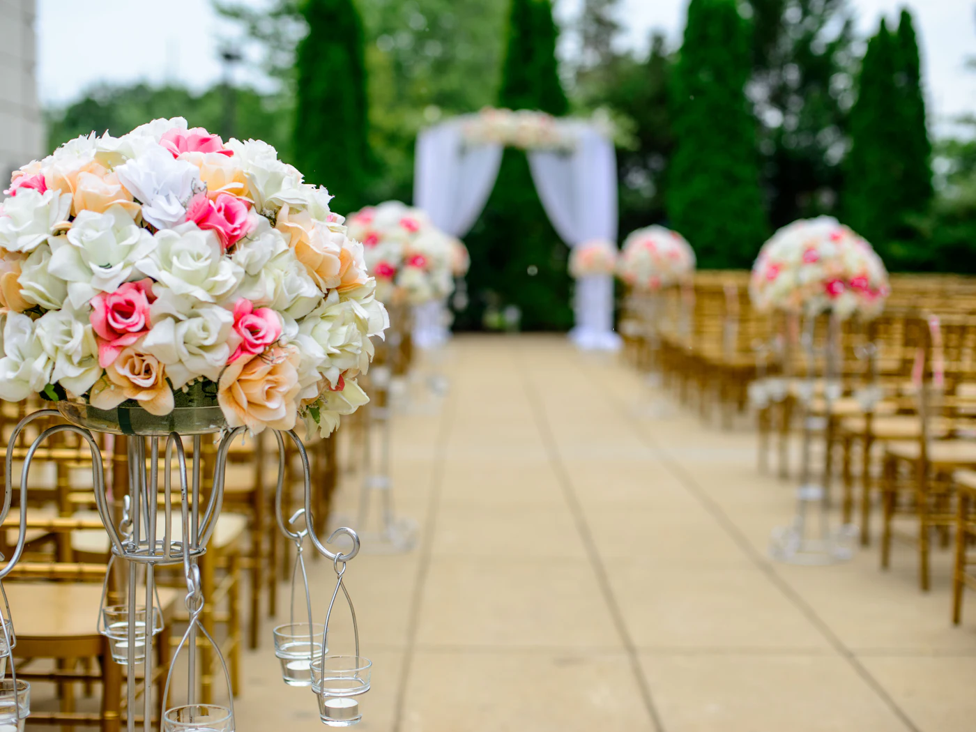 An outdoor ceremony aisle lined with floral arrangements and gold chairs